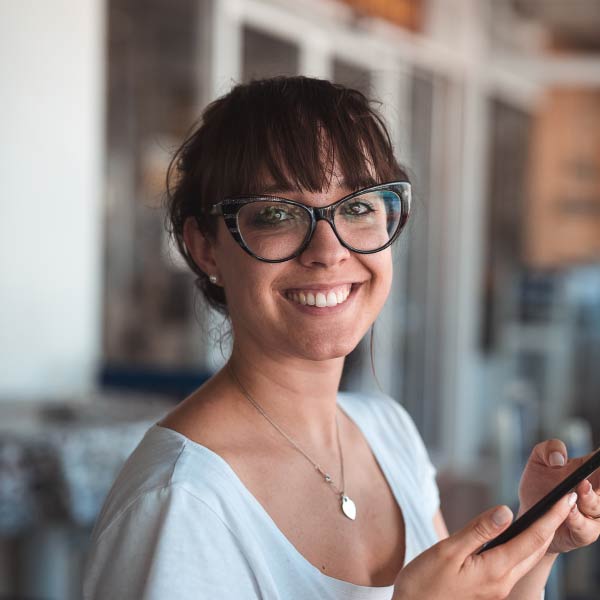 Smiling Maria Donald wearing glasses and holding a phone - Supply Chain Transparency