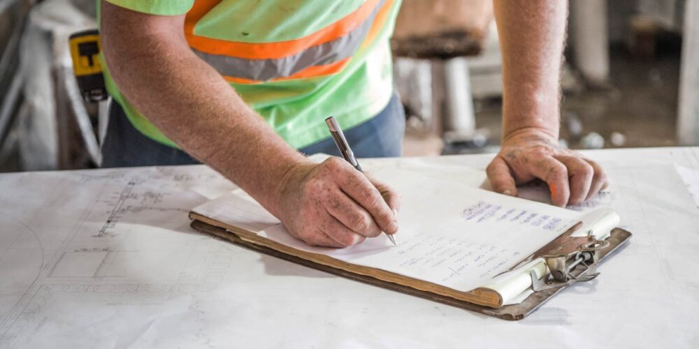 Construction worker reviewing blueprints and making notes on a clipboard. - Supply Chain Transparency