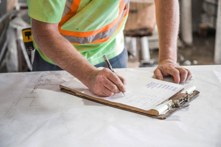 Construction worker reviewing blueprints and making notes on a clipboard. - Supply Chain Transparency