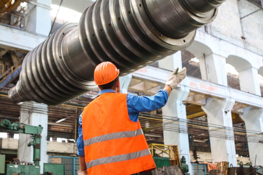 Worker in safety gear directs the movement of a large industrial component during a manufacturing process. - Supply Chain Transparency