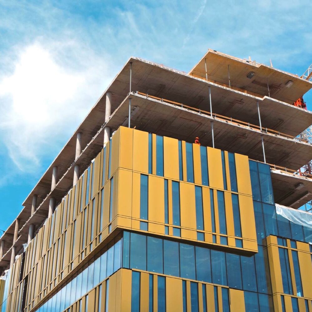 Modern building under construction, featuring yellow facade and large windows. Cranes are visible on the site. - Supply Chain Transparency