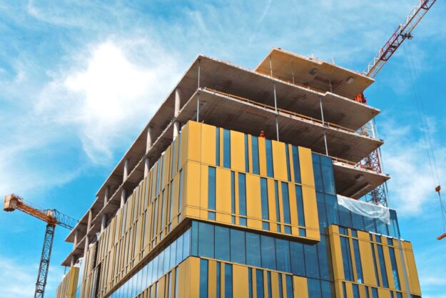 Modern building under construction, featuring yellow facade and large windows. Cranes are visible on the site. - Supply Chain Transparency