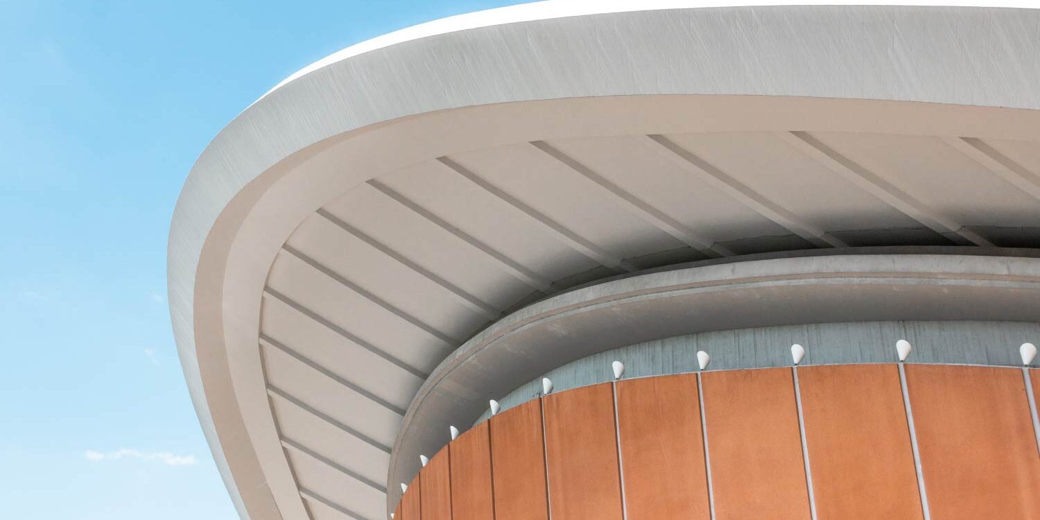 Modern building's curved roof and orange facade against a blue sky. - Supply Chain Transparency