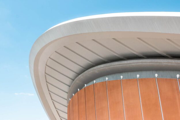 Modern building's curved roof and orange facade against a blue sky. - Supply Chain Transparency