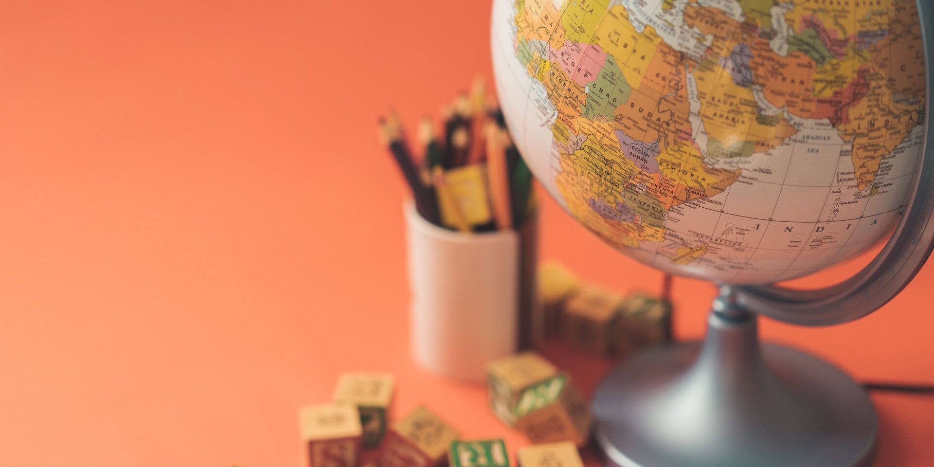 “The Impact of Globalization on International Trade” Globe, alphabet blocks, and colored pencils on orange background. Illustrates globalization's impact on education and trade. - Supply Chain Transparency