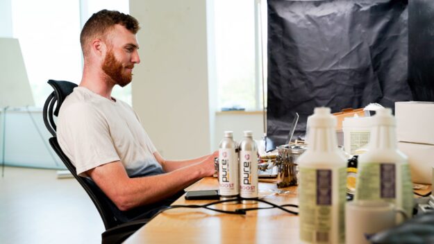 The Influence of Globalization on Supply Chain Strategies Man working at desk with laptop, surrounded by product packaging and Pure Boost cans. - Supply Chain Transparency