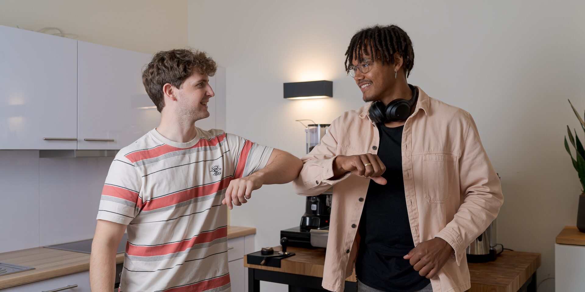 Two men elbow bumping, practicing social distancing in a kitchen. Communicating supply chain transparency. - Supply Chain Transparency