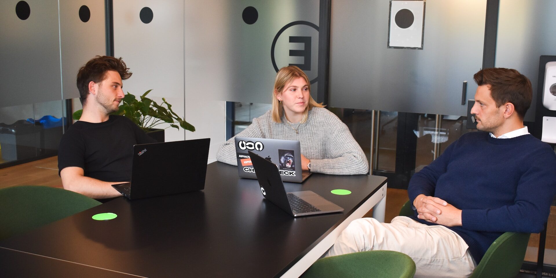 Three colleagues collaborate around a table, reviewing laptops during a business meeting. - Supply Chain Transparency