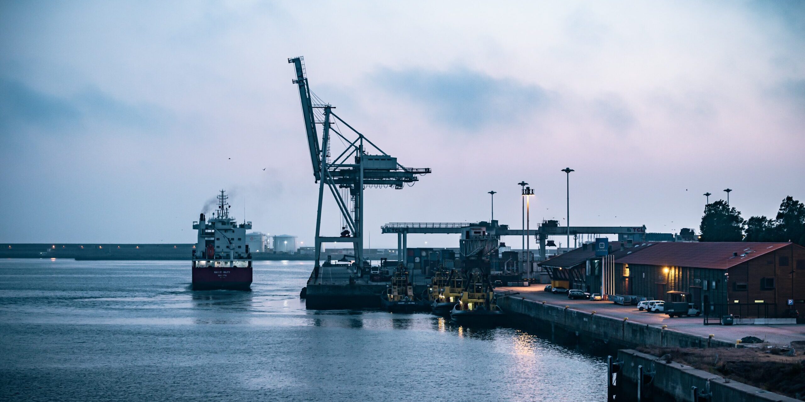 Supply Chains in International Trade: Challenges and Strategies Cargo ship at port with cranes during twilight. Illustrates international trade supply chain. - Supply Chain Transparency