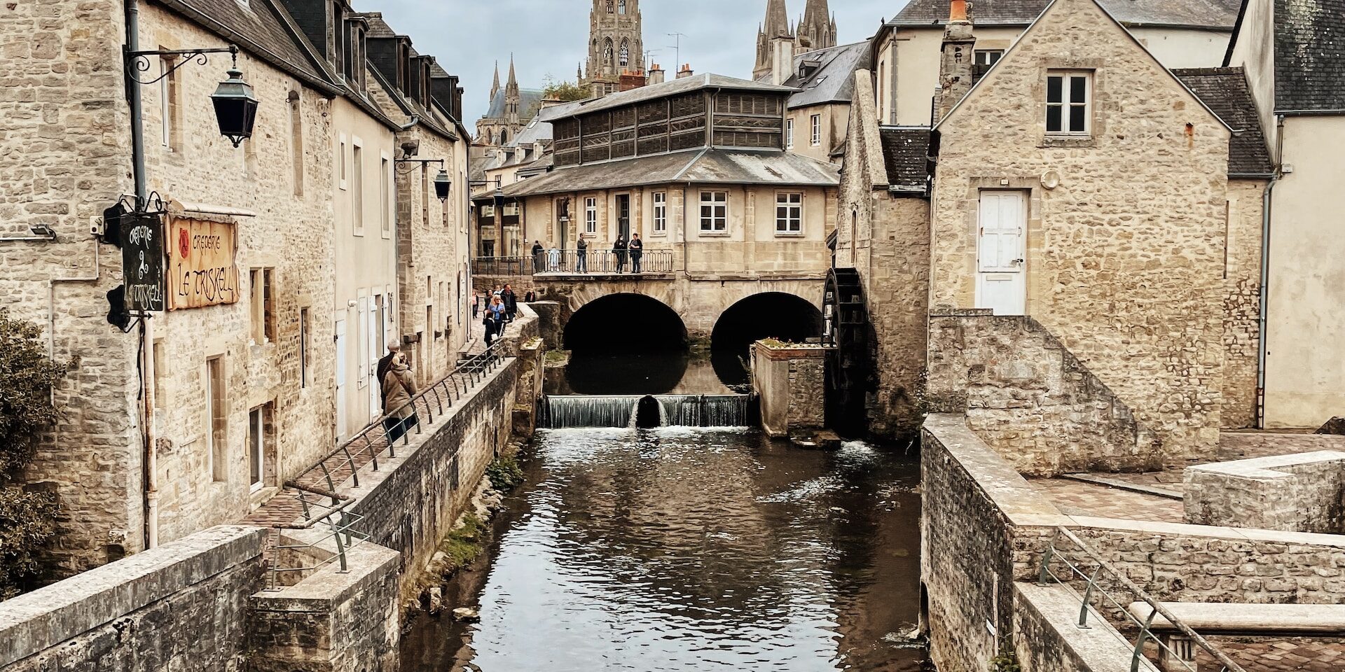 Supply Chain Forensics: Investigating and Resolving Fraudulent Activities Stone buildings line a canal with a water wheel, reflecting the overcast sky and a distant cathedral. - Supply Chain Transparency