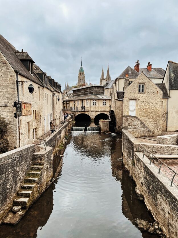 Supply Chain Forensics: Investigating and Resolving Fraudulent Activities Stone buildings line a canal with a water wheel, reflecting the overcast sky and a distant cathedral. - Supply Chain Transparency