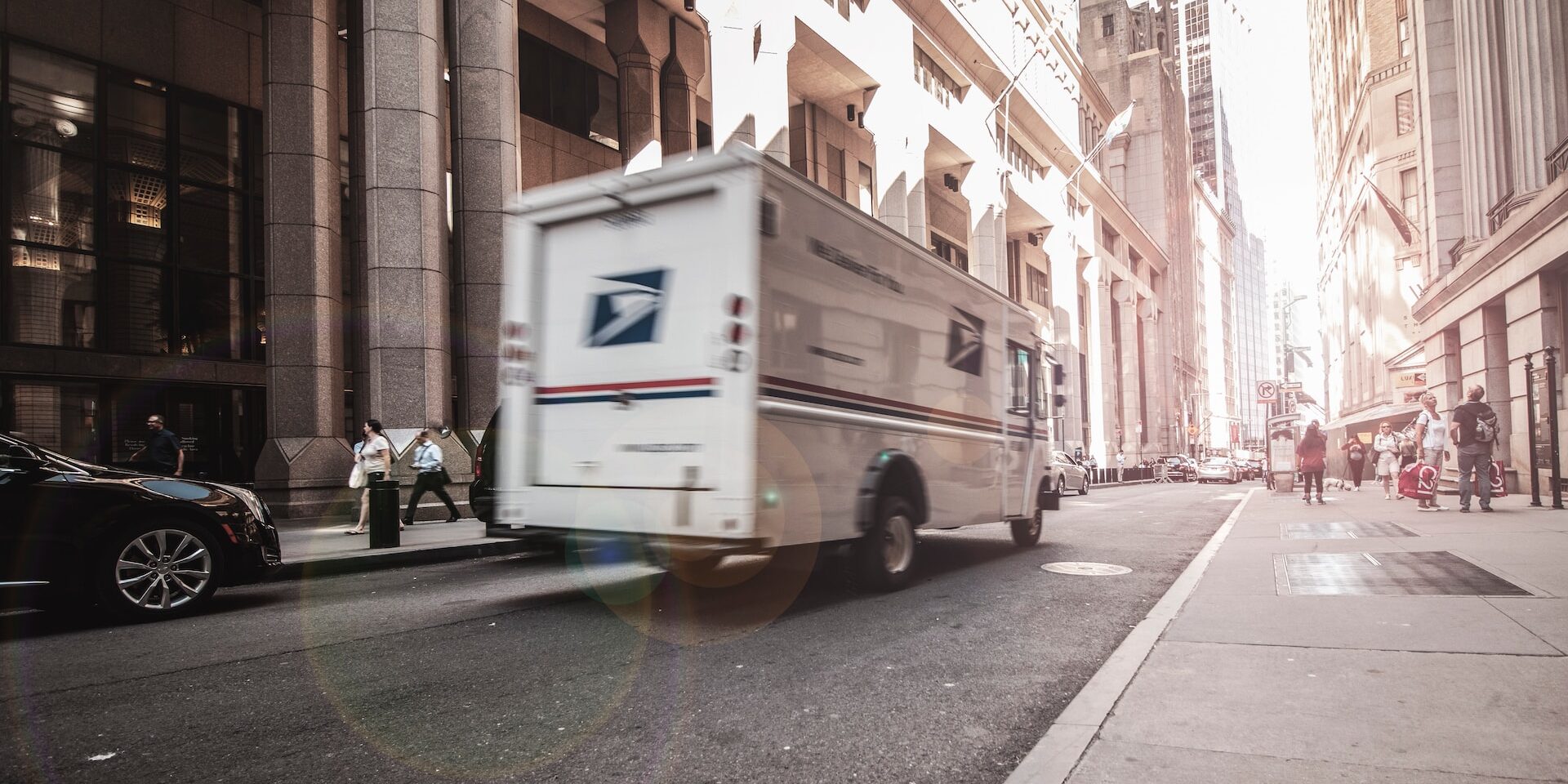 How to Build Resilient Supply Chains in the Face of Disruptions Blurred USPS truck driving down a city street, illustrating supply chain logistics. - Supply Chain Transparency