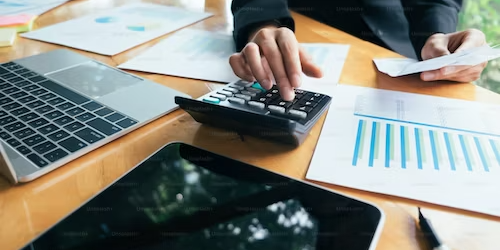 Businessperson reviewing financial data, using calculator and laptop for supply chain demand forecasting. - Supply Chain Transparency