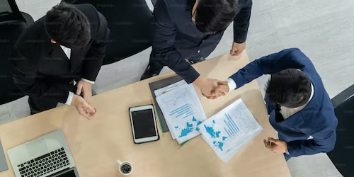 Supply Chain Talent Management: Attracting and Retaining Top Professionals Three businesspeople shaking hands at a meeting table, discussing supply chain talent management. - Supply Chain Transparency