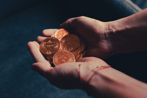 The Impact of Currency Exchange Rates on International Trade Close-up of hands holding a pile of gold Bitcoin coins. - Supply Chain Transparency