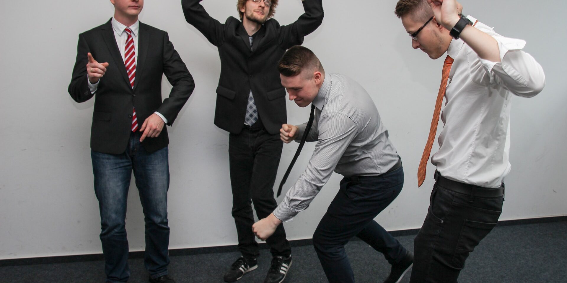 Four young businessmen playfully dancing, demonstrating adaptability and teamwork in a modern office setting. - Supply Chain Transparency