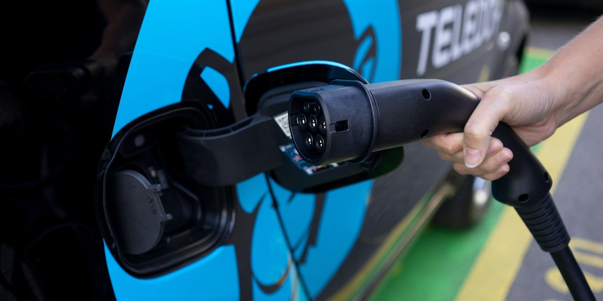 The Role of Technology in Driving Supply Chain Transparency Hand plugging in EV charging cable into electric car. Teleboy logo visible. - Supply Chain Transparency