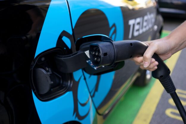 The Role of Technology in Driving Supply Chain Transparency Hand plugging in EV charging cable into electric car. Teleboy logo visible. - Supply Chain Transparency
