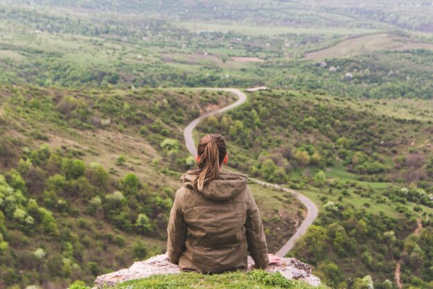 From Supplier to Shelf: Mapping the Journey towards Transparent Supply Chains Woman sits on a cliff overlooking a winding road, contemplating the journey ahead. Transparent supply chain concept. - Supply Chain Transparency