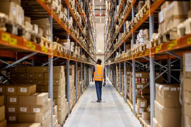 istockphoto-1581310056-612×612 Warehouse worker walking down aisle of stacked boxes. Supply chain innovation. - Supply Chain Transparency